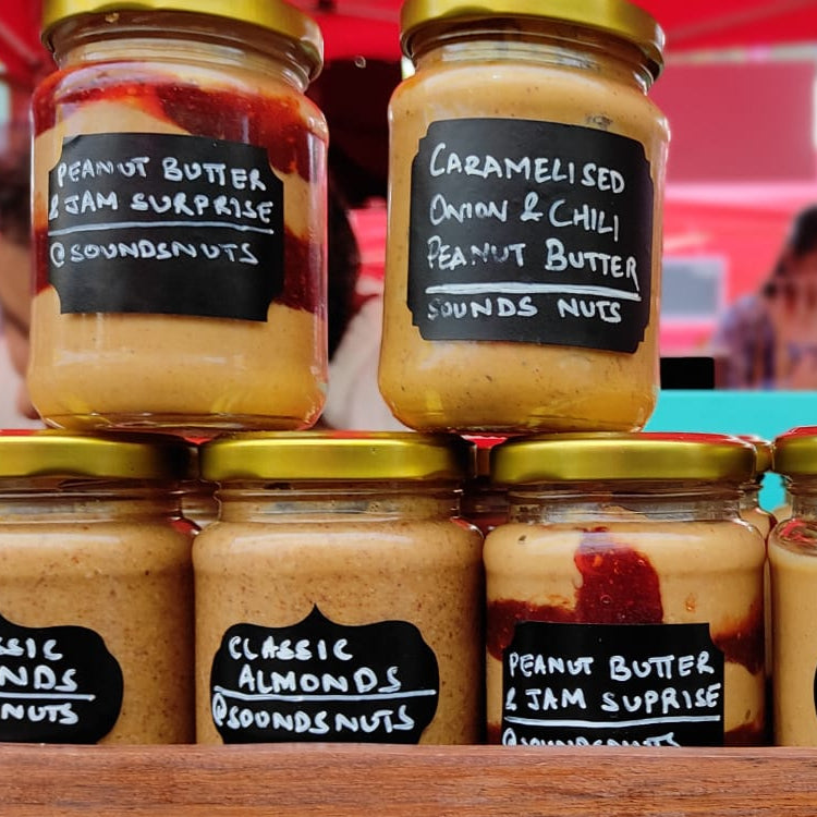 Jars of peanut butter with various flavors and labels on a wooden surface.