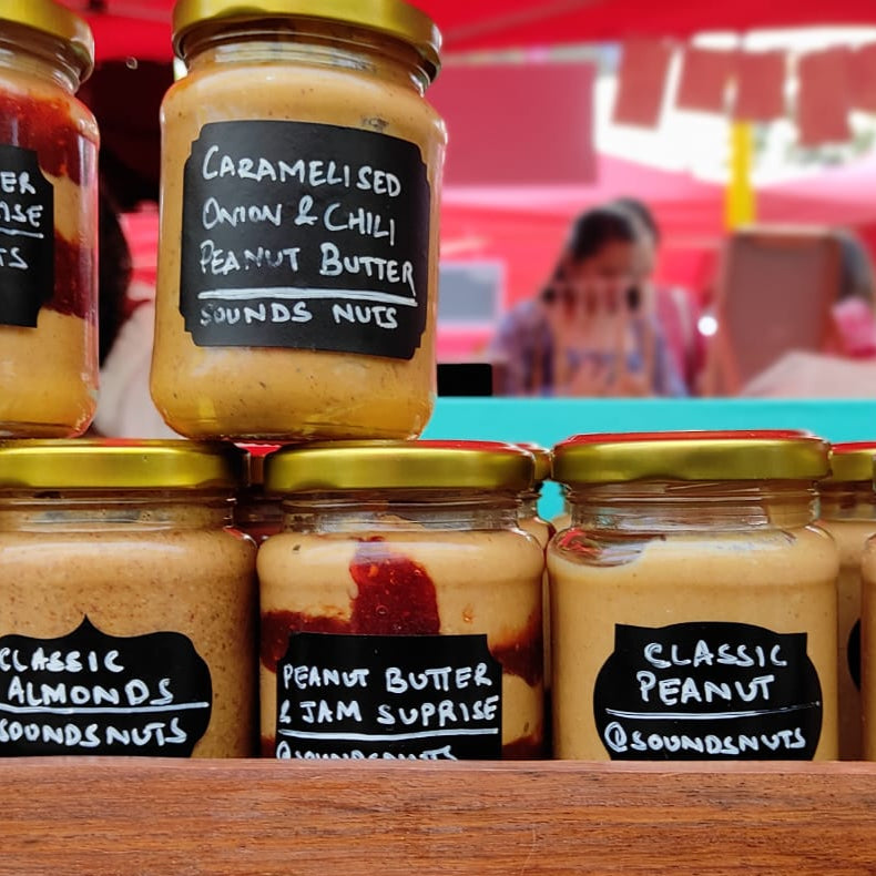 Jars of peanut butter and other spreads on a wooden stand with blurred background