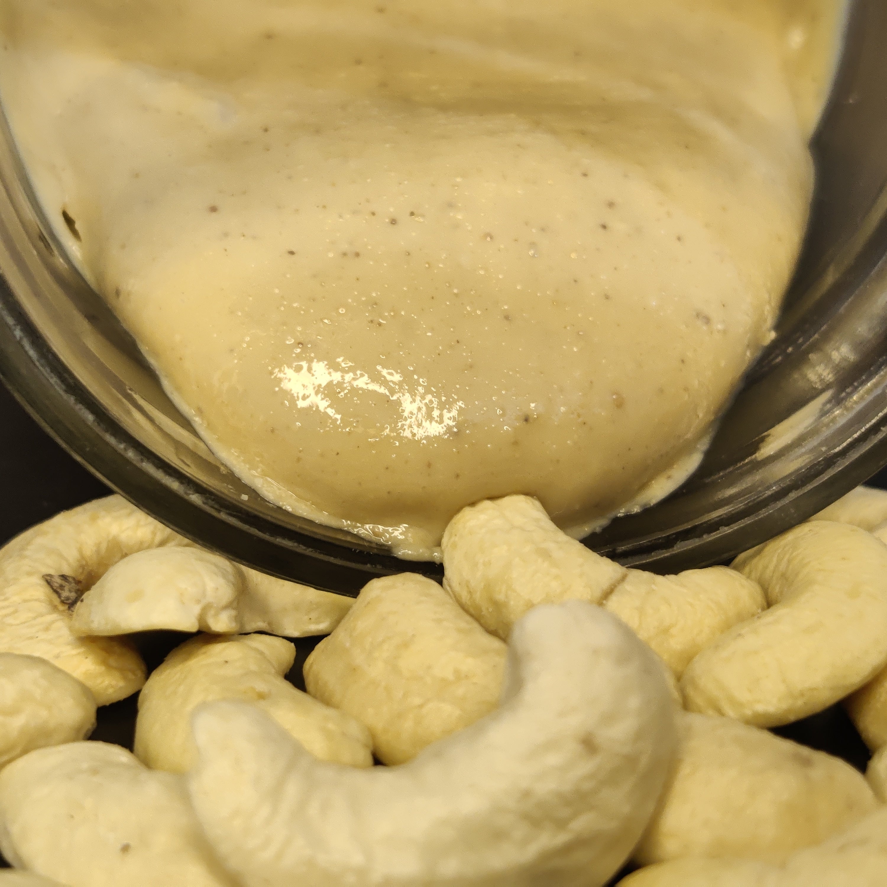 Cashew nuts with a creamy cashew butter spread on top in a glass bowl.