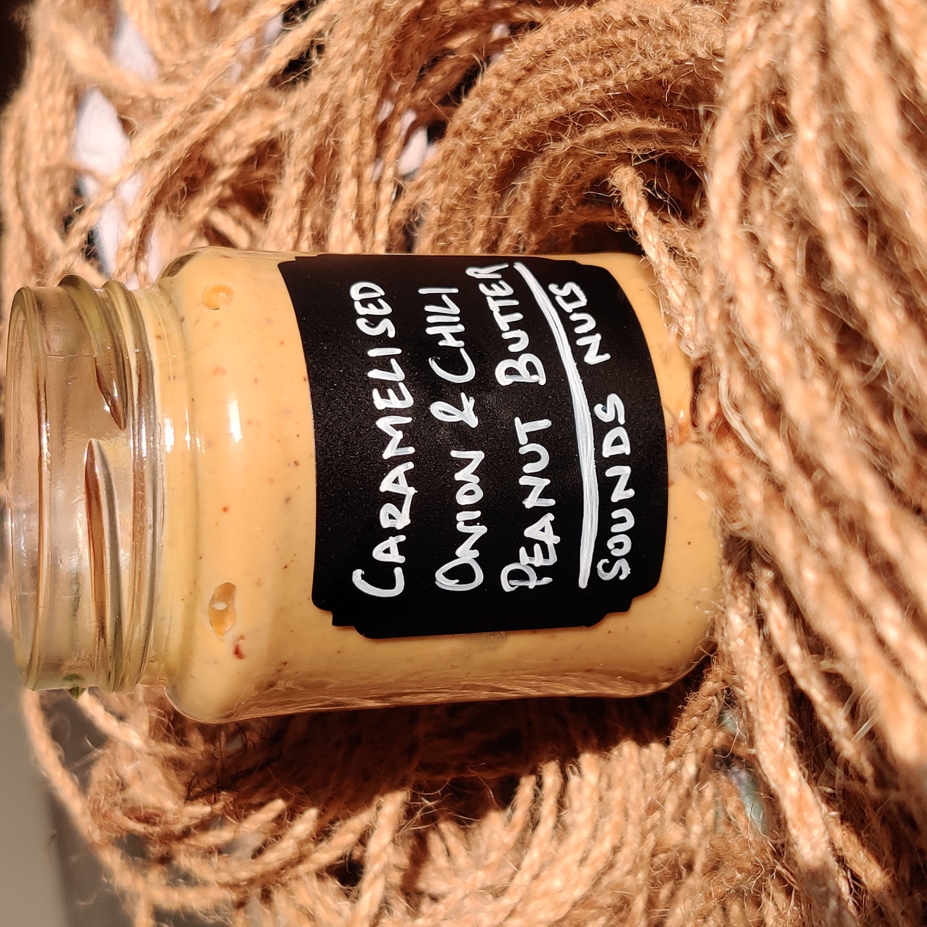 Jar of caramelized onion and chili peanut butter on a jute background