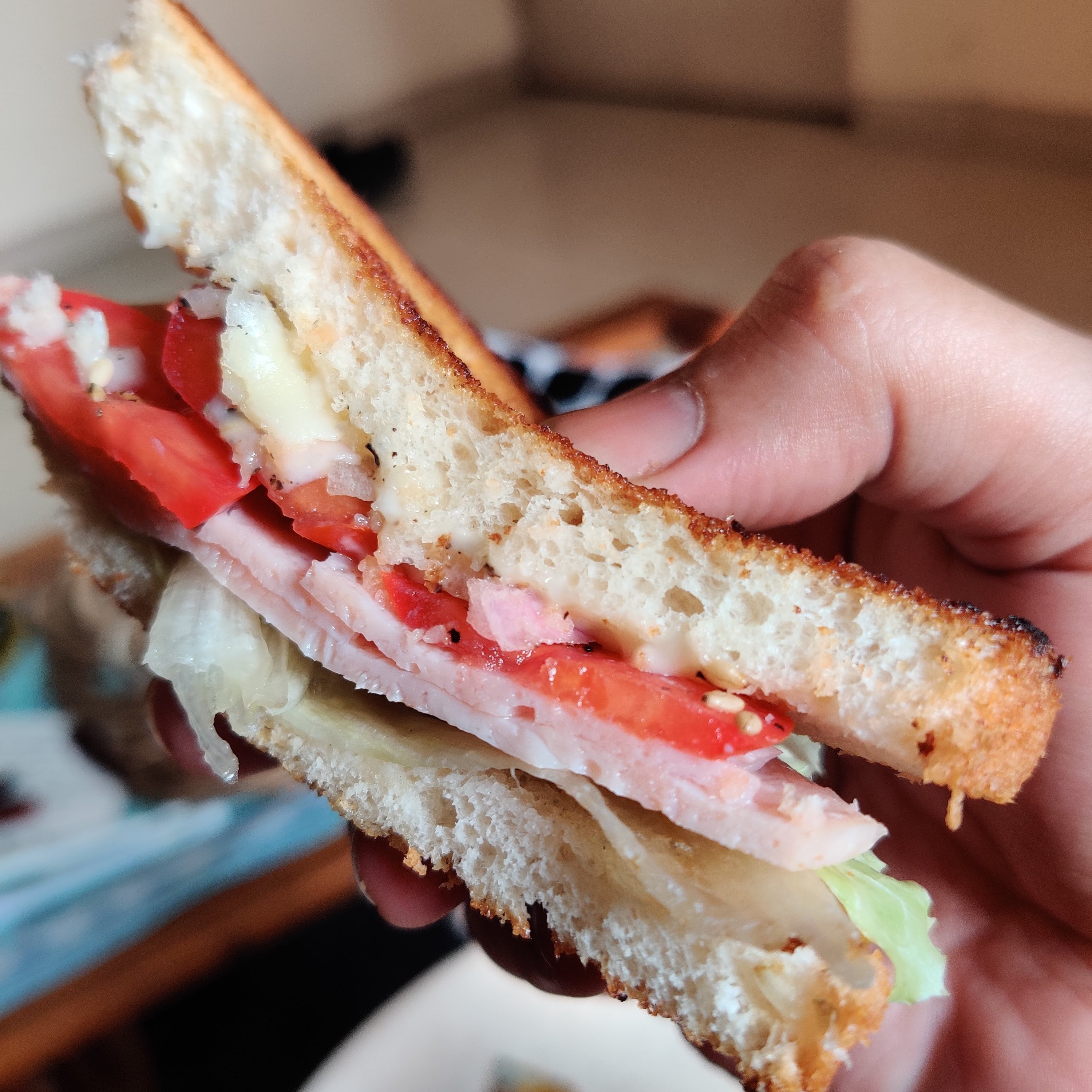 Hand holding a sandwich with visible layers of bread, tomatoes, Caramelized onion peanut butter and other ingredients.