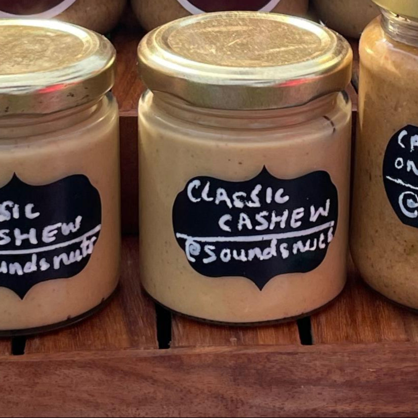 Three jars of cashew cream and butter with labels on a wooden surface